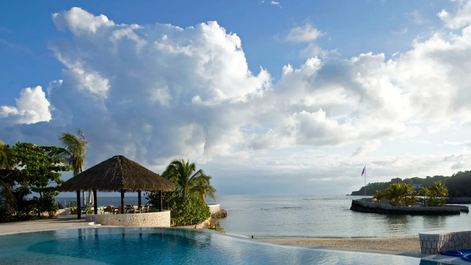 Wooden cottage at GoldenEye Hotel set among palms above a Caribbean cove at golden hour